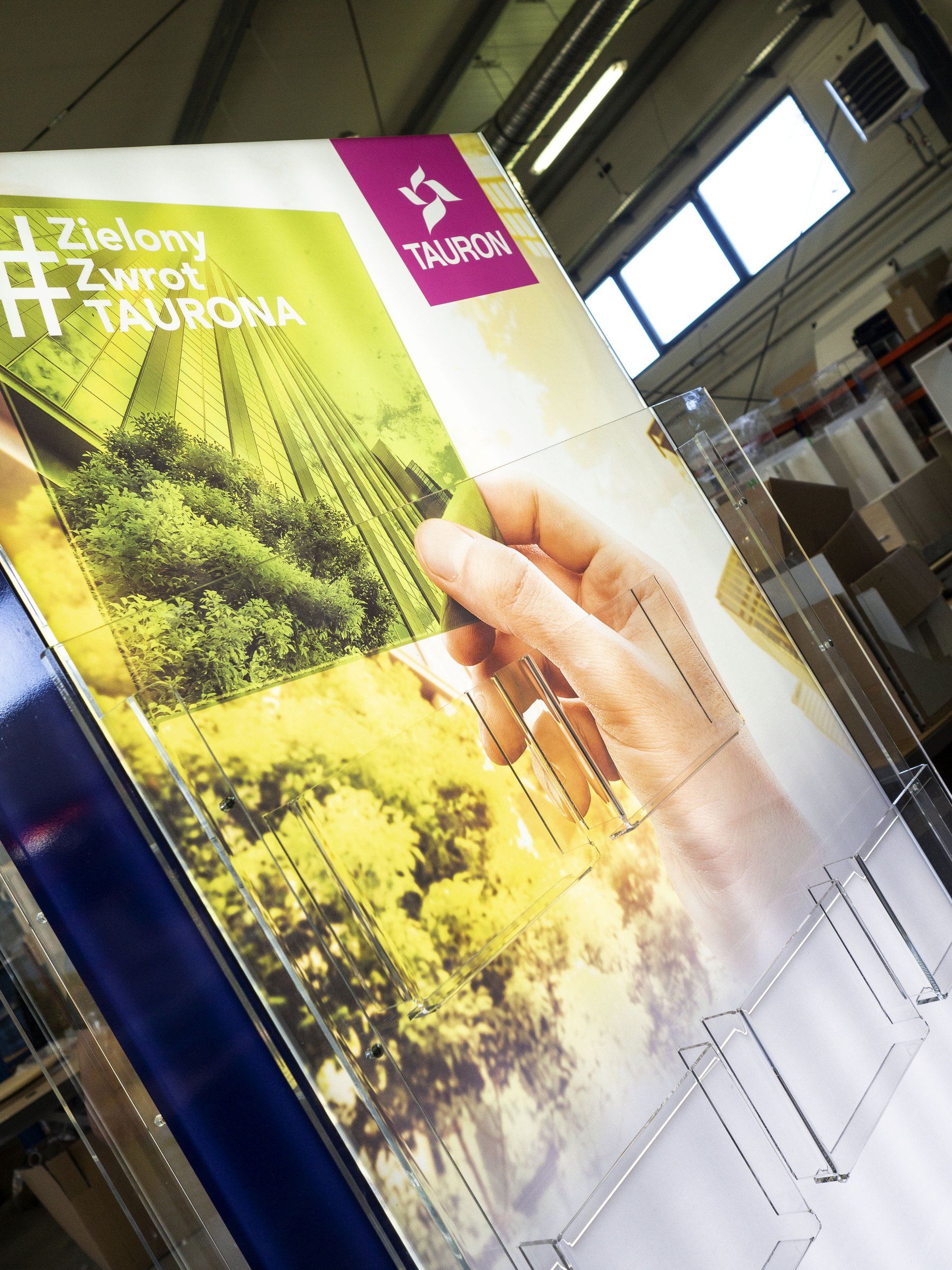 Detal standu TAURON w hali: grafika kampanii i kieszenie z przezroczystej plexi na katalogi